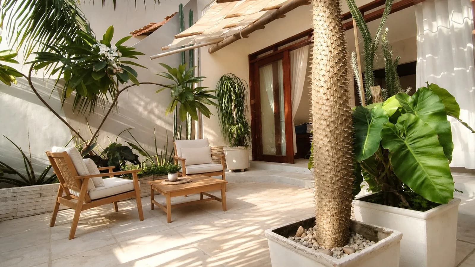 Pátio com pergolado e toldo, poltronas, plantas tropicais e portas de vidro da sala